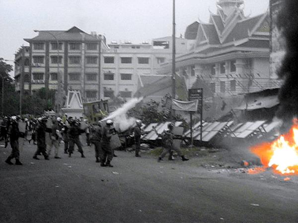 More tear gas is fired and, at center right, a helmeted policeman throws a rock at residents.